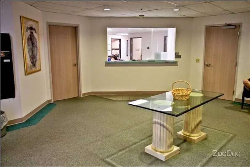 A waiting room at the office: a glass-topped table on two columns with a wicker basket, a service window and two wooden doors