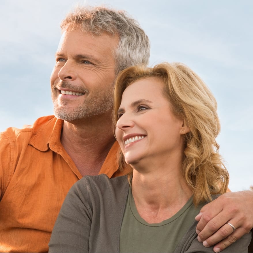 Stock photograph of models: a smiling middle-aged couple sit close together outdoors under a bright sky, his arm around her