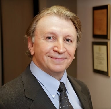 Dr. Blair Kranson, MD, smiling, in a dark suit and tie, with framed certificates on the wall behind him